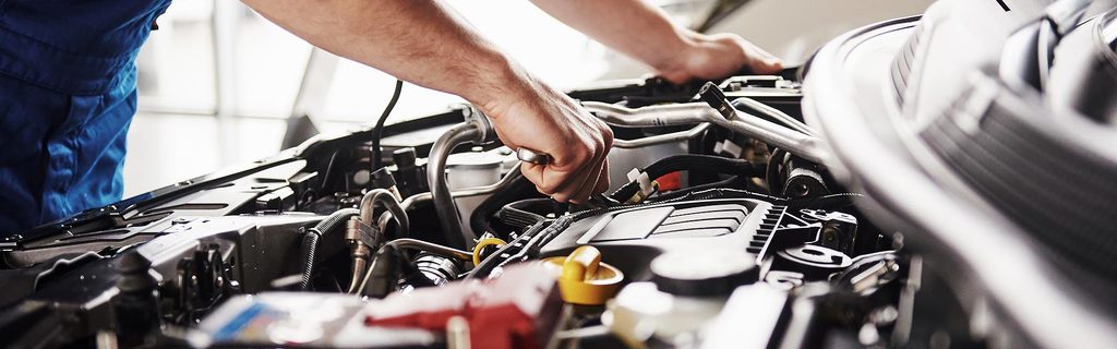 A certified GMC Service Center mechanic is shown in a close-up as he inspects a vehicle engine.